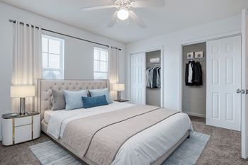 A bedroom with a large bed, a ceiling fan, and a closet with clothes hanging.